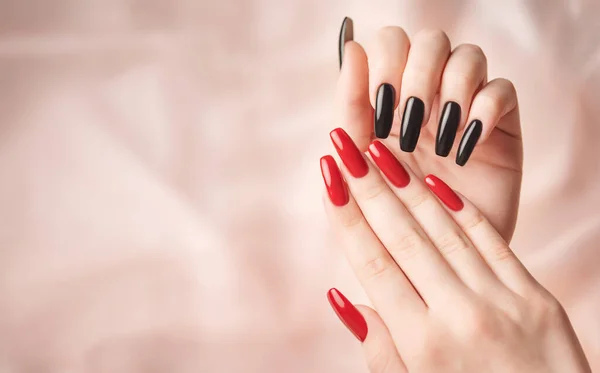 Hands of young girl with red  and black manicure on nails on beige silk  background