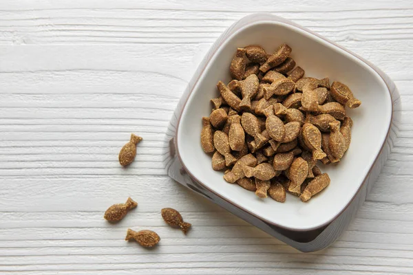 A bowl of dog food, dry puppy food in the shape of a fish on a wooden floor. Dry food in granules.