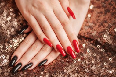 Hands of young girl with red  and black manicure on nails on sequins  background