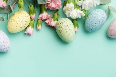 Easter colored eggs and a bouquet of white and pink carnations with eucalyptus branches on a soft green background. Festive background.