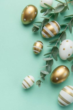 Easter eggs painted in gold and eucalyptus branches on a soft green background. Festive background