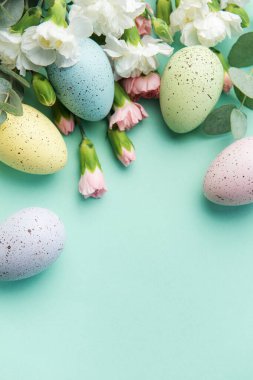 Easter colored eggs and a bouquet of white and pink carnations with eucalyptus branches on a soft green background. Festive background.