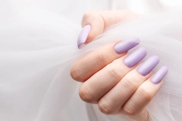 Girl\'s hands with a soft purple manicure. White background of silk and tulle. Concept of beauty and care.