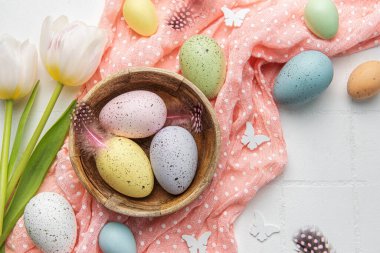 Easter background with colorful eggs in bowl and pink tulips on a white  background. Top view 