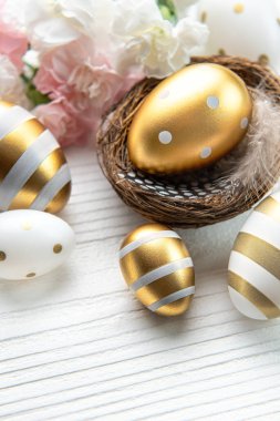 Nest with Easter eggs painted golden colors and pink tulips on a white wooden background. Top view. Space for text.