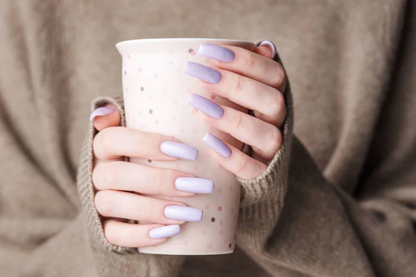 Trendy female manicure. Woman's hands with  violet manicure  holding a cup of tea.  Cozy winter or autumn concept.