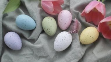Pink decorative feathers fall on a table with colored Easter eggs. The concept of preparing for the Easter holiday