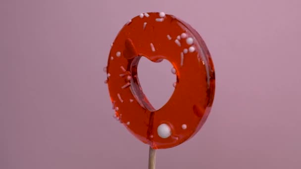 甘いキャンディー ピンクの背景に回転スティック上のロリポップレッドハート バレンタインデーのコンセプト — ストック動画