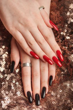 Hands of young girl with red  and black manicure on nails on sequins  background