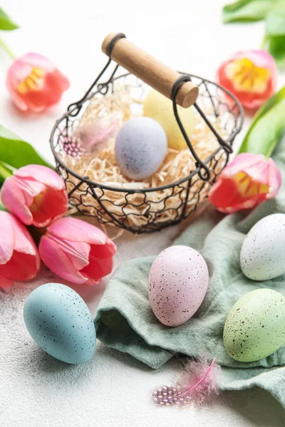 Basket with Easter eggs painted  pastel colors and pink tulips on a concrete background. Top view. Space for text.