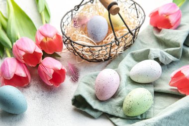 Basket with Easter eggs painted  pastel colors and pink tulips on a concrete background. Top view. Space for text.