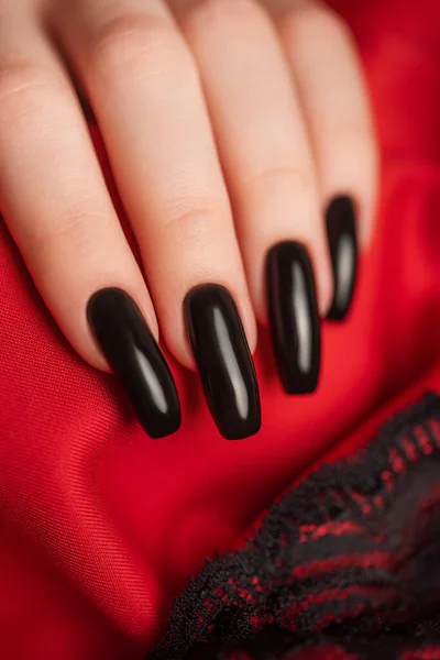 Hand of young girl with  black manicure on nails on red background with black lace