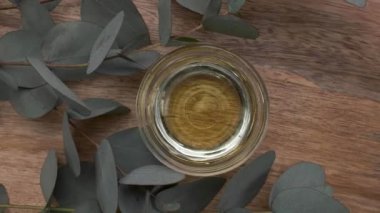 Okaliptüs yağıyla dolu bir kase ve ahşap bir arka planda yapraklar dönüyor. Okaliptüs özü, aromatik gerekli yağ. Doğal kozmetikler. Üst görünüm.