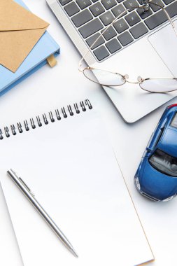 Modern white office desk table with laptop, notebook, toy car and other supplies. Blank copy space for  the text. Top view, flat lay. Concept of selling contracts, car dealerships offer