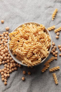 Gri bir arka planda nohut fasülyesi fusilli makarna. Çiğ makarna ve nohut ile kase. Glütensiz makarna..