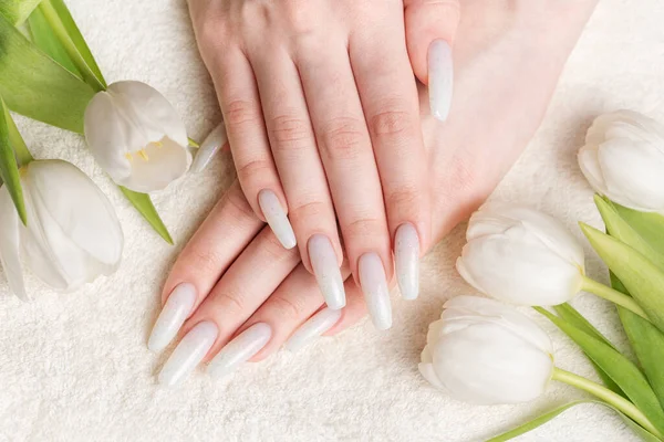Female hand with spring nail design. White nail polish manicure. Female model hand with perfect manicure hold white tulip flowers on towel background