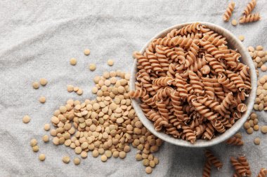 Gri bir arka planda yeşil mercimek fusilli makarna. Bir kase çiğ makarna ve yeşil mercimek. Glütensiz makarna..