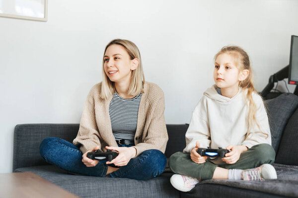 Young women and little girl joyful playing video games with controller console. Two sisters playing games. 