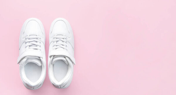 White children's sneakers on a pink background with copy space. Banner.