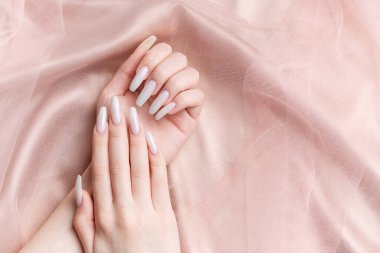 Manikürlü bir kadının elleri, tırnakları beyaz bir renge boyanır. Pembe ipek arkaplan