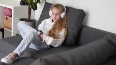 Kulaklıklı ve dijital tabletli müzik dinleyen küçük bir kız. Tablet oyunu, kulaklıklar ve rahatlama çocuk oyunları, eğlenmek veya online oyunlar oynamak veya müzik dinlemek