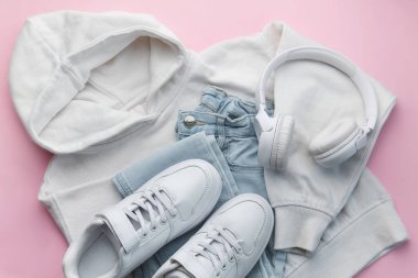 Çocuk kıyafetleri, aksesuarlar, ayakkabılar, sweatshirt, kot pantolon, spor ayakkabı, pembe arka planda kulaklık. Gençler için giysi. Üst manzara, düz yatış. Moda rengi