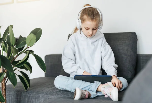 Pieni Tyttö Makaa Sohvalla Elektroninen Tabletti Kuuntelee Musiikkia Valkoiset Kuulokkeet — kuvapankkivalokuva