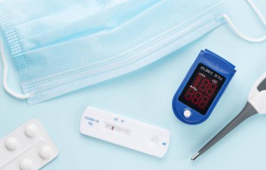 Koronavirüsün önlenmesi ve tedavisi için ilk yardım çantası. Mavi arka planda maske, test, nabız oksimetresi ve ilaç.