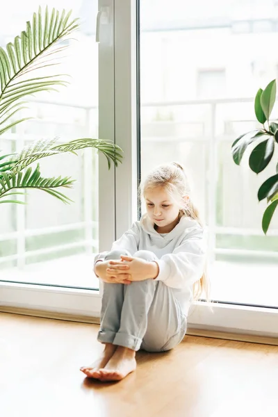stock image Lonely sad little girl sitting by the window.