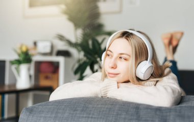 Kulaklıklı genç sarışın kadın müzik dinliyor ve evde dinleniyor..