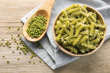 Eski ahşap arka planda Mung fasulyeli fusilli makarna. Çiğ makarna ve yeşil fasulyeli kase. Glütensiz makarna..