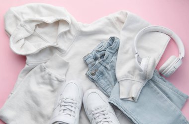 Çocuk kıyafetleri, aksesuarlar, ayakkabılar, sweatshirt, kot pantolon, spor ayakkabı, pembe arka planda kulaklık. Gençler için giysi. Üst manzara, düz yatış. Moda rengi