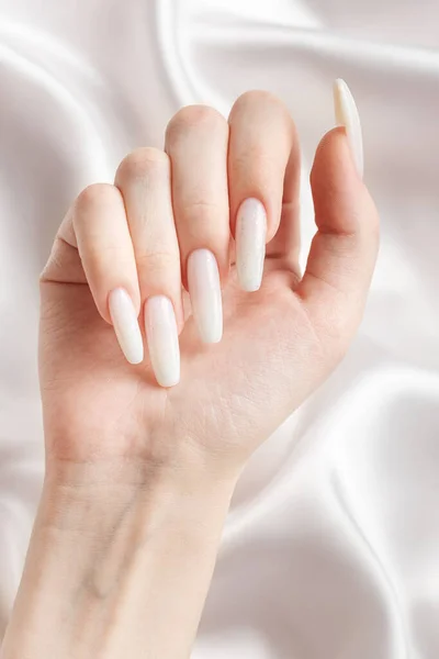 一个女人的手 指甲上有一个修指甲 指甲被漆成了白色 白色丝绸背景 — 图库照片