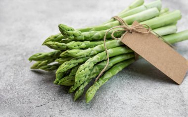 Gri beton arka planda boş etiketli taze yeşil kuşkonmaz. Düz yatıyordu