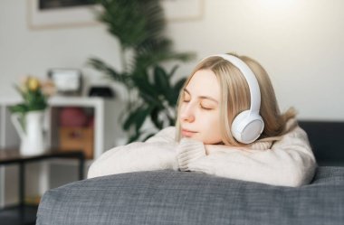 Kulaklıklı genç sarışın kadın müzik dinliyor ve evde dinleniyor..