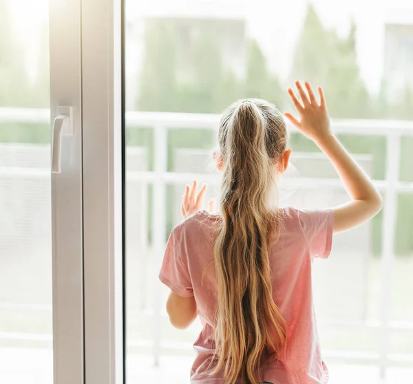 stock image Lonely little girl  looking out window, standing at home alone. 