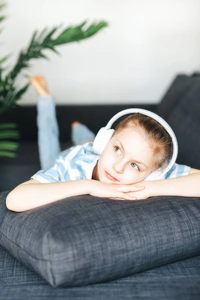 stock image Cute little girl listening to music in headphones while lying on the sofa at home.