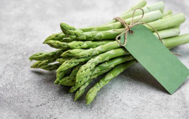 Gri beton arka planda boş etiketli taze yeşil kuşkonmaz. Düz yatıyordu