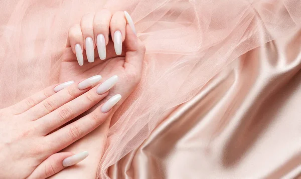 一个女人的手 指甲上有一个修指甲 指甲被漆成了白色 粉红丝质背景 — 图库照片