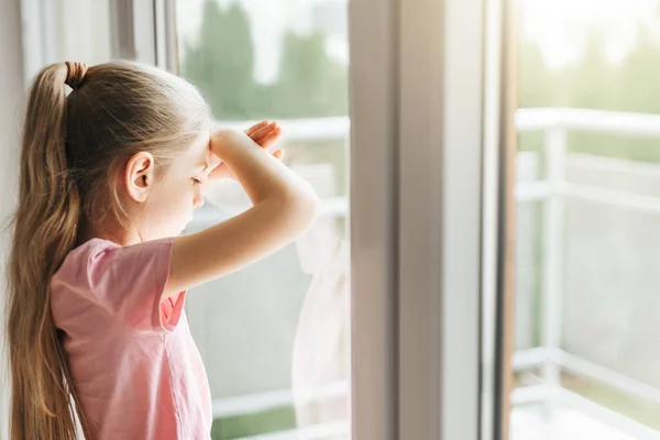 stock image Lonely little girl  looking out window, standing at home alone. 