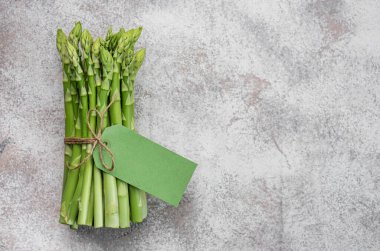 Gri beton arka planda boş etiketli taze yeşil kuşkonmaz. Düz yatıyordu