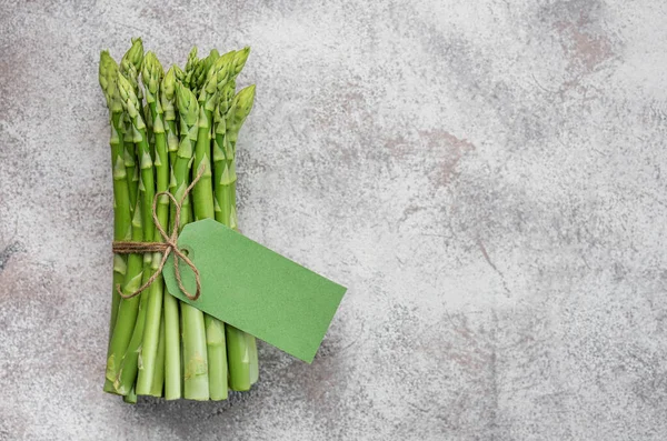 Gri beton arka planda boş etiketli taze yeşil kuşkonmaz. Düz yatıyordu