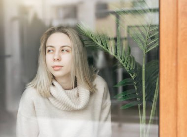 Pencerenin yanındaki üzgün kız bir şey düşünüyor. Stresli bayan kendini yalnız hissediyor.