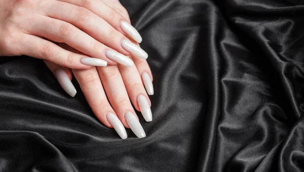 一个女人的手 指甲上有一个修指甲 指甲被漆成了白色 黑丝背景 — 图库照片