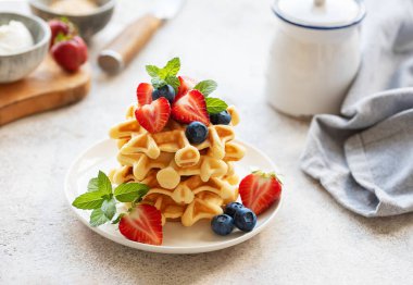 Beton gri arka planda çilek ve yaban mersinli taze pişmiş waffle. Ev yapımı pişirme..