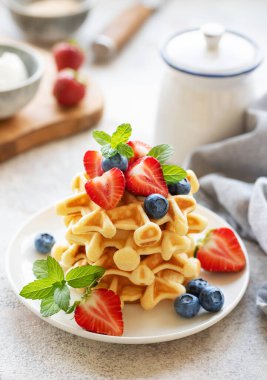 Beton gri arka planda çilek ve yaban mersinli taze pişmiş waffle. Ev yapımı pişirme..