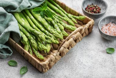 Bir grup çiğ kuşkonmaz, gri beton arka planda farklı baharatlar içerir.