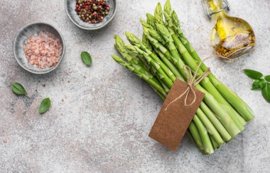 Bir grup çiğ kuşkonmaz, gri beton arka planda farklı baharatlar içerir.