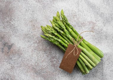 Gri beton arka planda boş etiketli taze yeşil kuşkonmaz. Düz yatıyordu