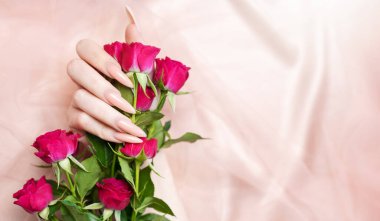 Zarif pastel pembe doğal manikür. Pembe ipek arka planda gülleri olan kadın elleri.